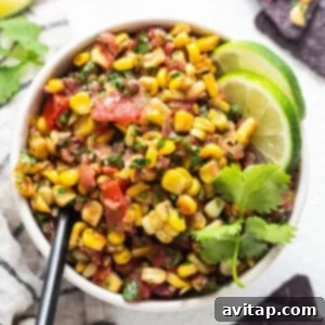 mexican corn salad in a white bowl with limes and tortilla chips.