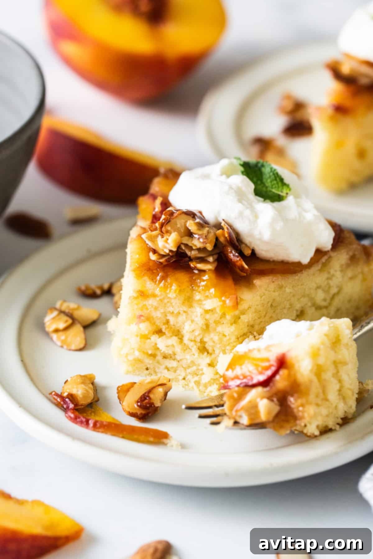 Golden Peach Upside Down Cake 2 A slice of peach cake with whipped cream and almonds on a plate, highlighting the delicious layers.