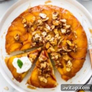 Golden Peach Upside Down Cake 13 A peach upside down cake on a plate with a slice taken out, adorned with whipped cream.
