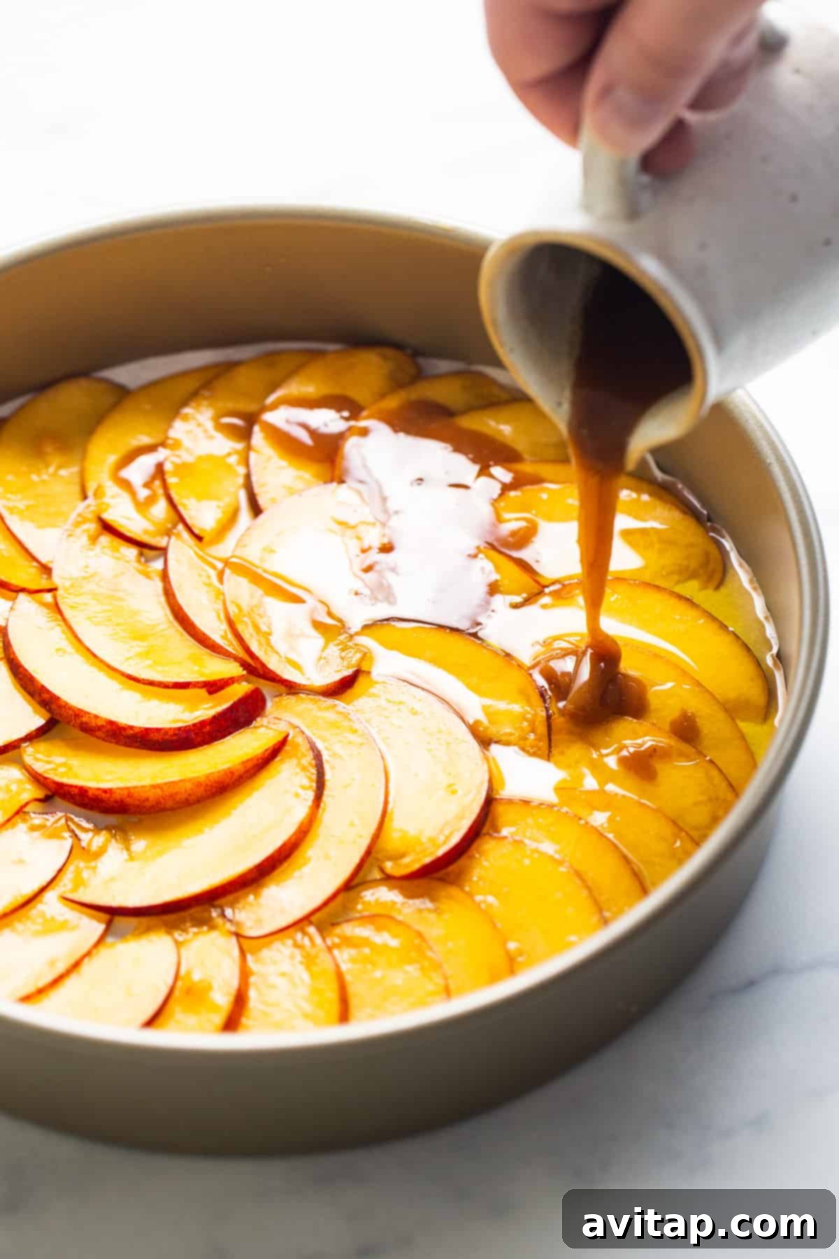 Golden Peach Upside Down Cake 3 A person pouring rich caramel sauce over a layer of sliced peaches arranged in a cake pan.