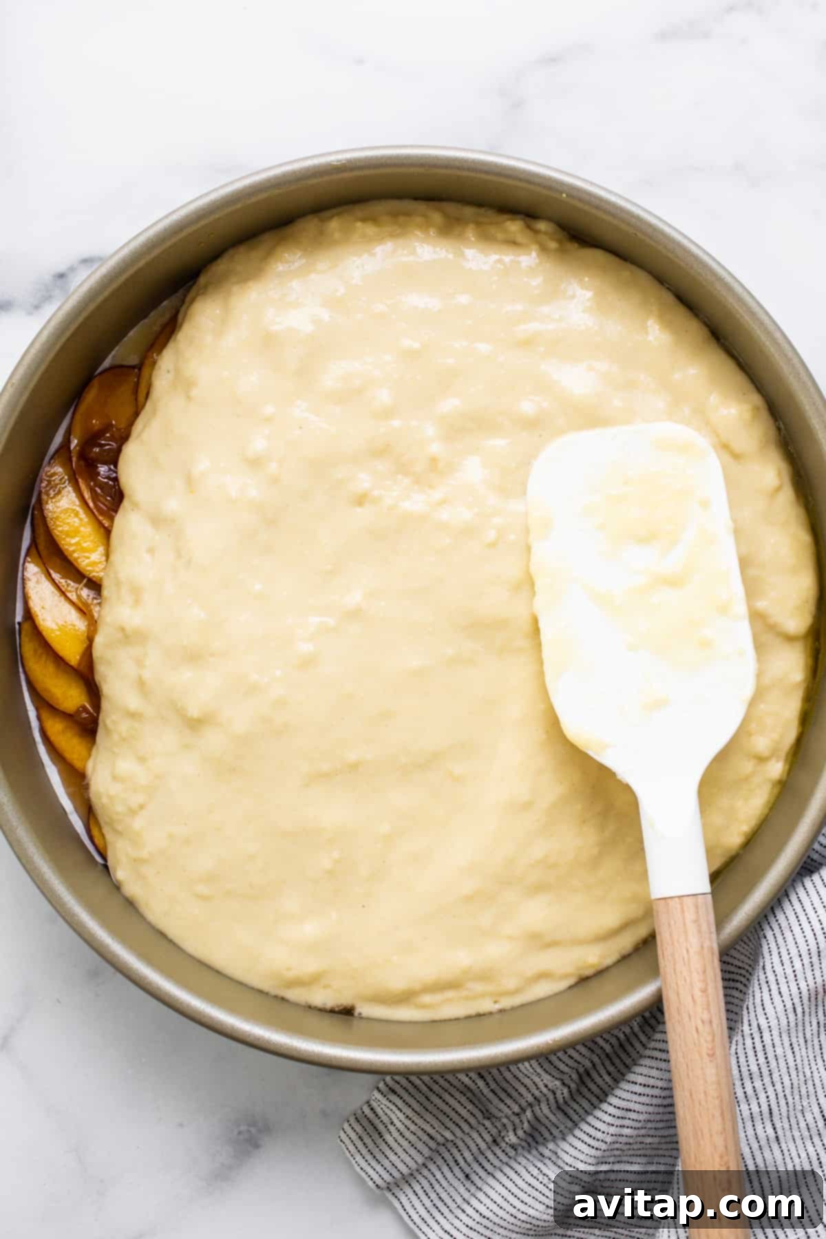 Golden Peach Upside Down Cake 4 A freshly baked peach cake still in its pan, showing the golden-brown crust, with a spatula nearby.