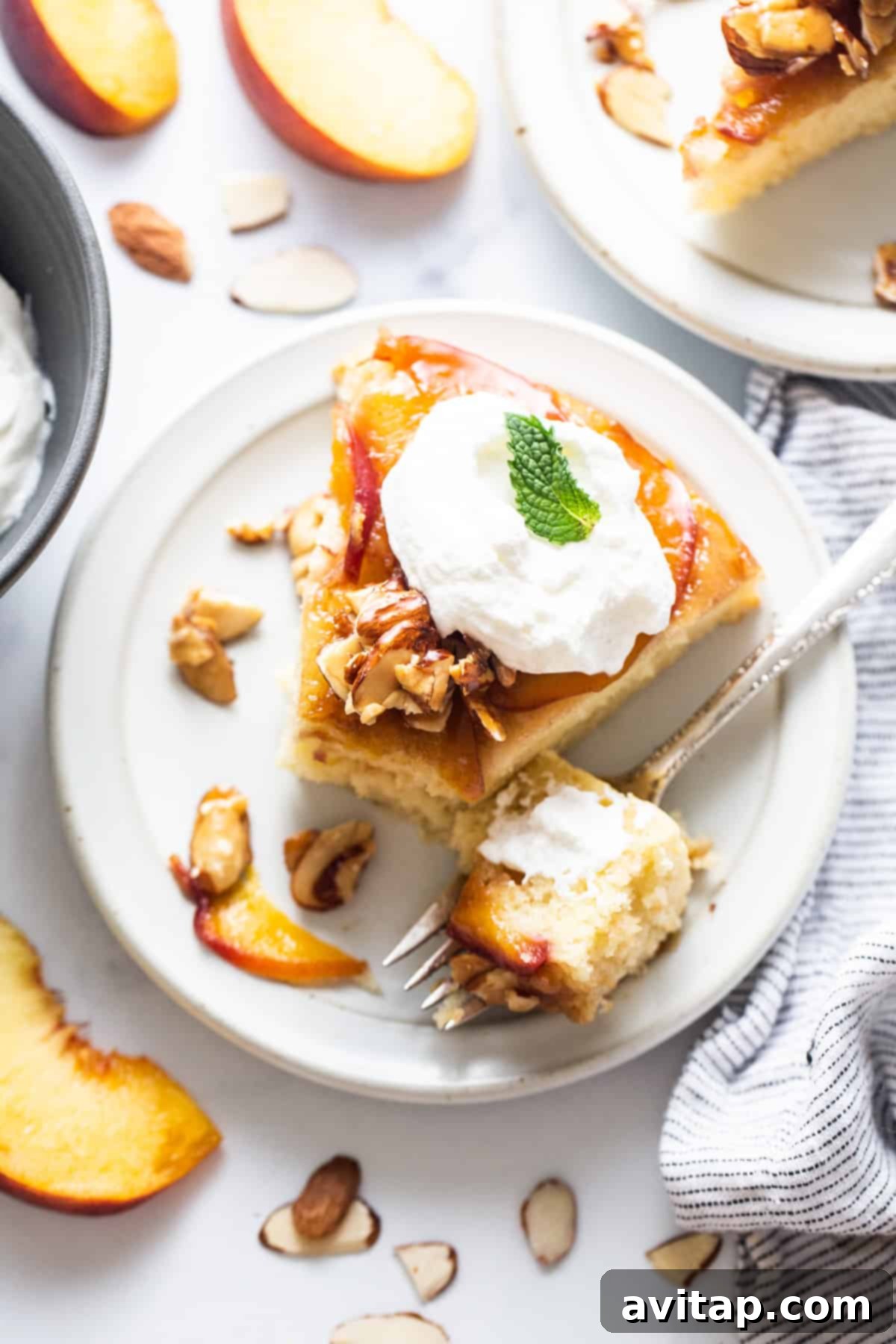 Golden Peach Upside Down Cake 7 Another enticing slice of peach cake, beautifully presented with a dollop of whipped cream and scattered almonds.