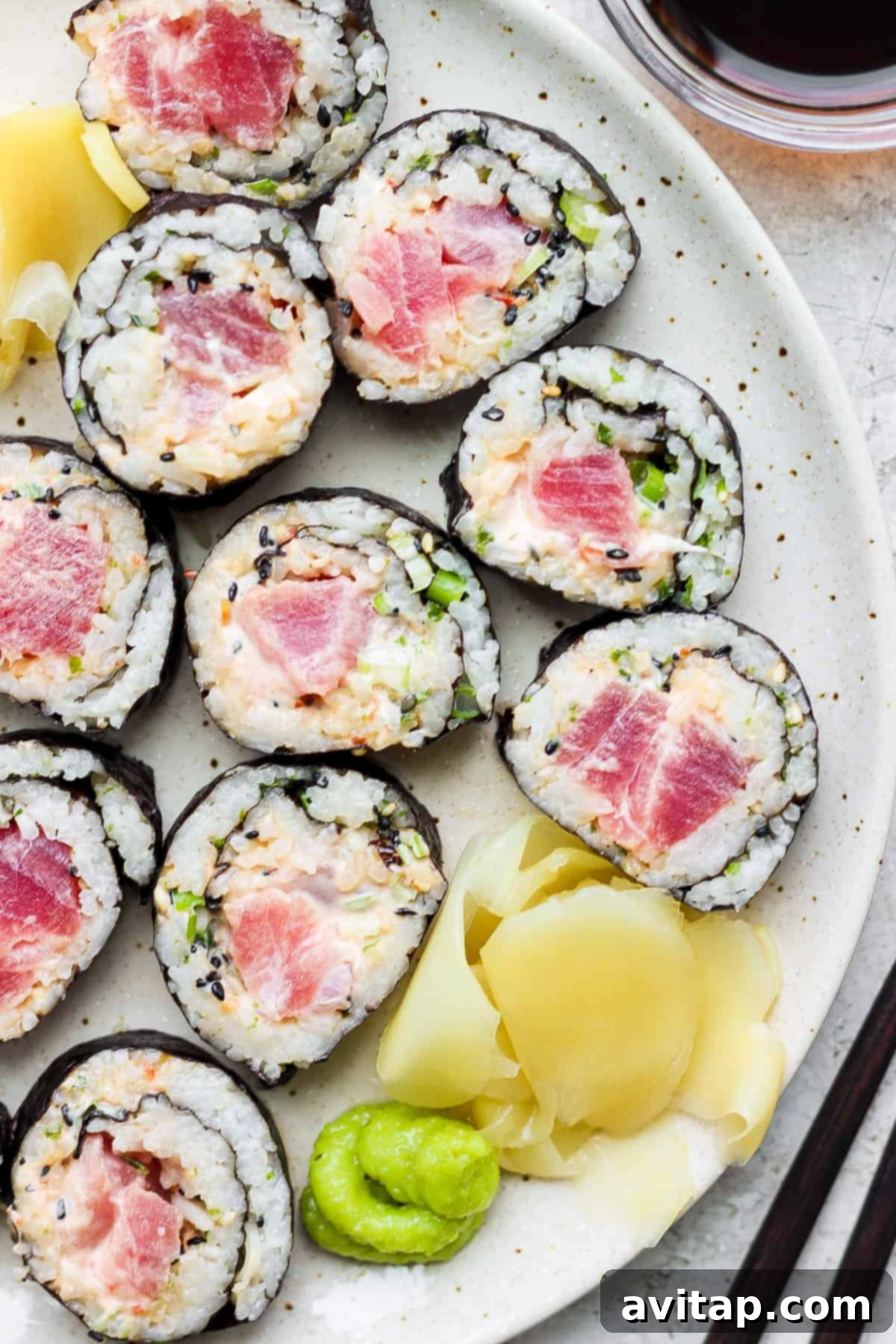 A beautifully plated spicy tuna sushi roll with fresh cucumber slices and a drizzle of sauce.