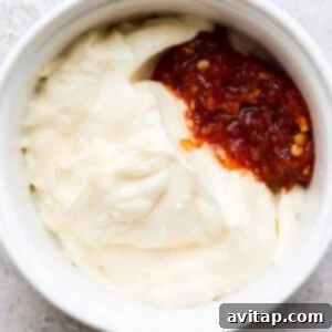 A bowl of creamy mayonnaise blended with red chili garlic sauce, forming a vibrant spicy mayo.