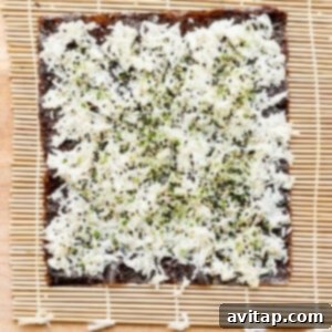 A nori sheet covered with rice and topped with tuna, furikake, green onions, and spicy mayo, ready to be rolled.