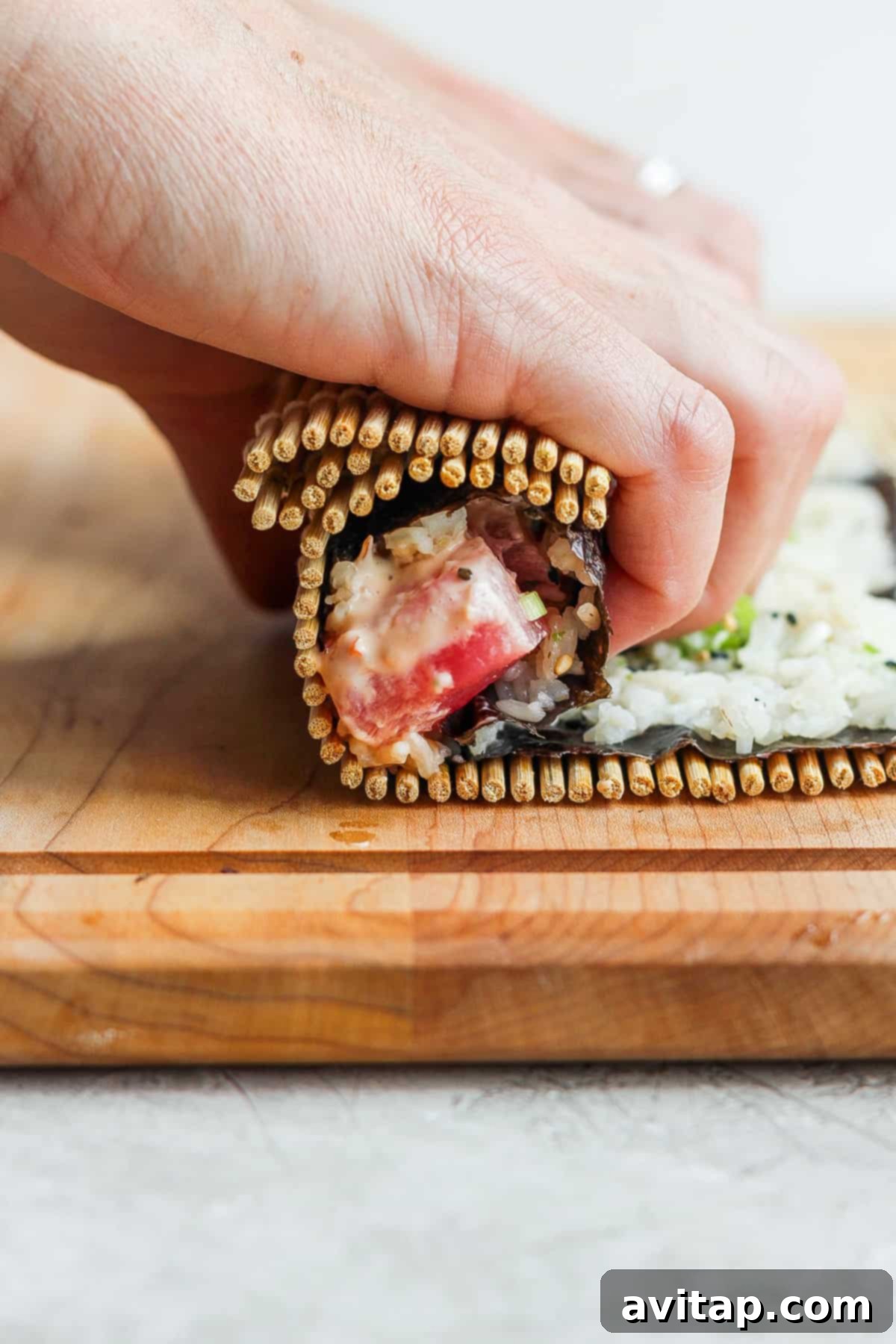 A person meticulously cutting a freshly rolled sushi log into individual pieces on a wooden board.
