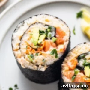 Two generous sushi burritos on a plate with a lemon wedge and a side of soy sauce.