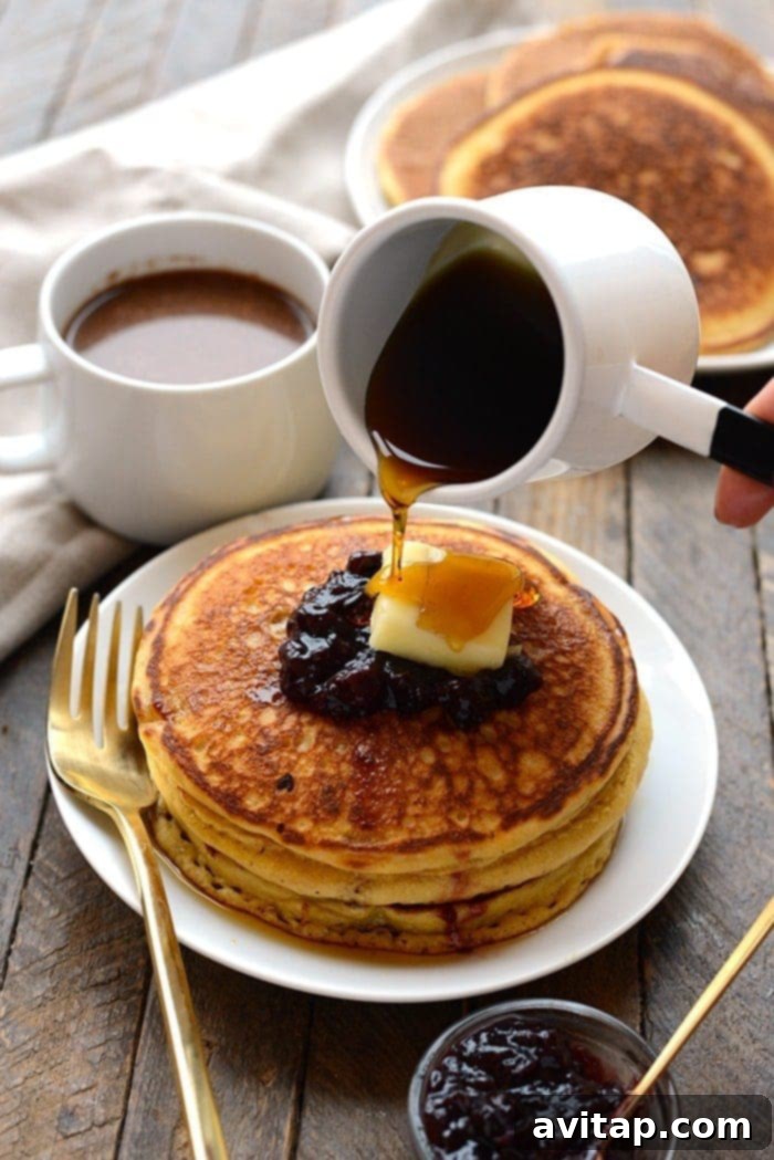 Stack of fluffy whole wheat cornmeal pancakes on a plate, topped with fresh berries and maple syrup, ready for a delicious breakfast.