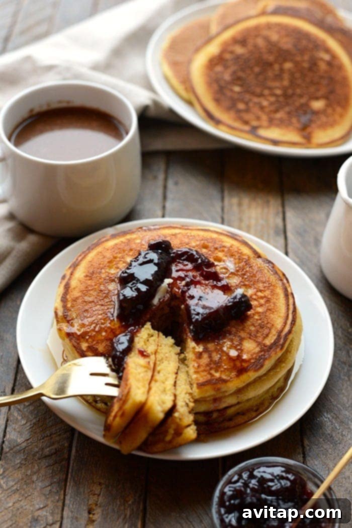 A hand reaching for a piece of freshly cooked whole wheat cornmeal pancake, showing the fluffy texture and golden-brown edges.