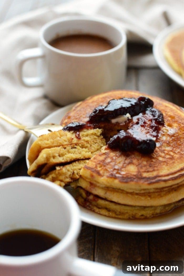 A beautifully presented stack of whole wheat cornmeal pancakes, garnished with fresh fruit, on a rustic breakfast table.