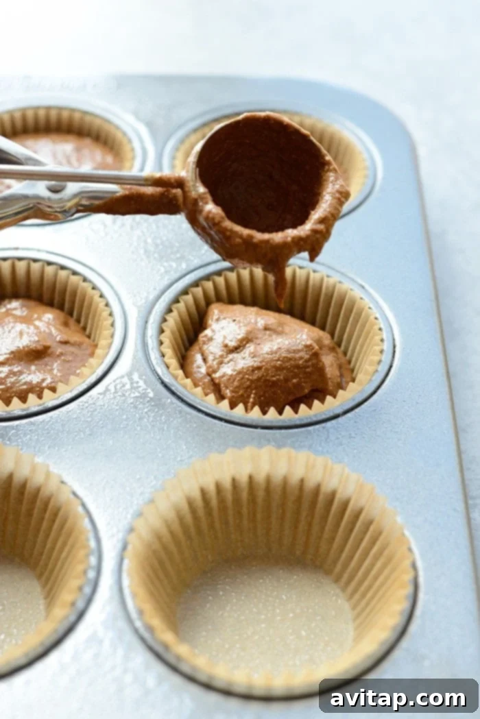 Thick, chocolatey pumpkin muffin batter being carefully scooped into a paper-lined muffin tin, promising delicious results.
