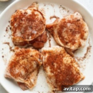 Perfectly Seared Cast Iron Chicken Thighs 10 Four seasoned chicken thighs on a white plate, ready for cooking.
