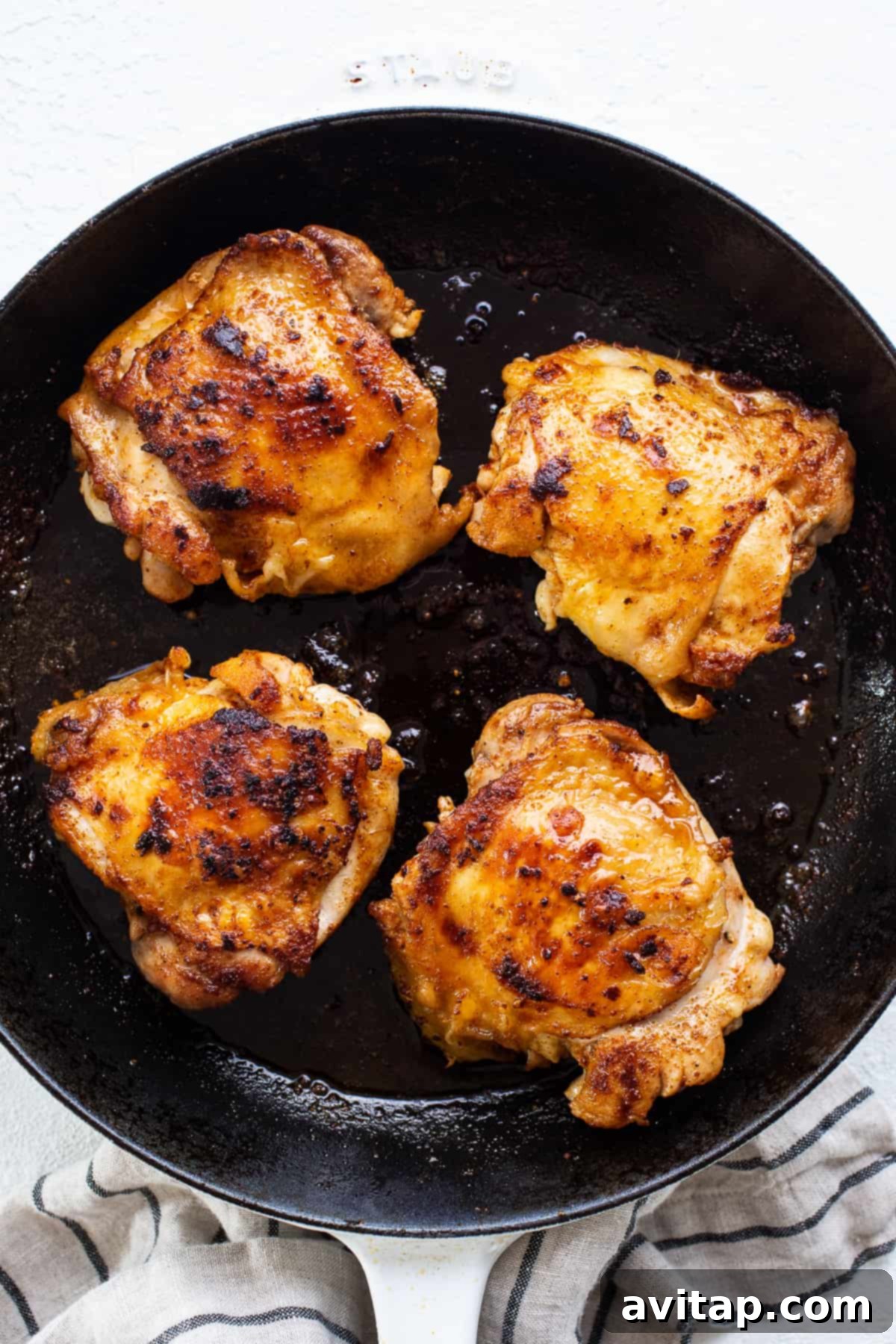 Perfectly Seared Cast Iron Chicken Thighs 4 An open cast iron skillet with golden-brown chicken thighs nestled in a rich simmering sauce, fresh from the oven.