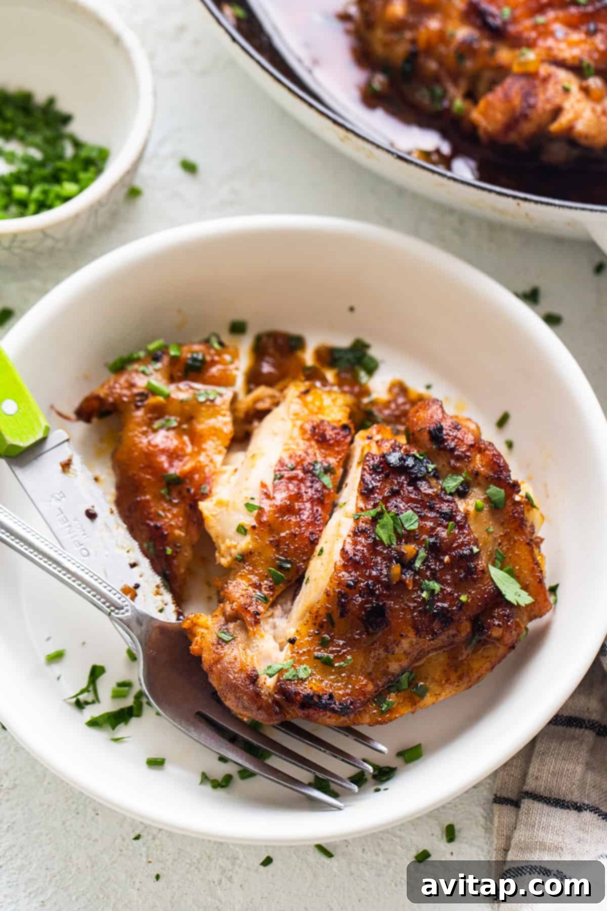 Perfectly Seared Cast Iron Chicken Thighs 7 A single perfectly crispy chicken thigh on a white plate, ready to be enjoyed with a fork.