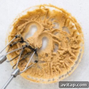 Wet muffin ingredients, including brown sugar and butter, being creamed to a light and fluffy consistency with an electric mixer.