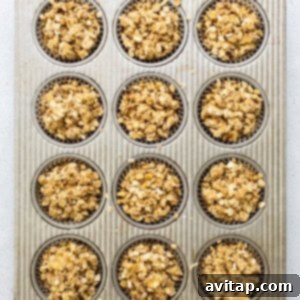 A muffin tin filled with unbaked apple muffins, each generously topped with streusel and ready for the oven.