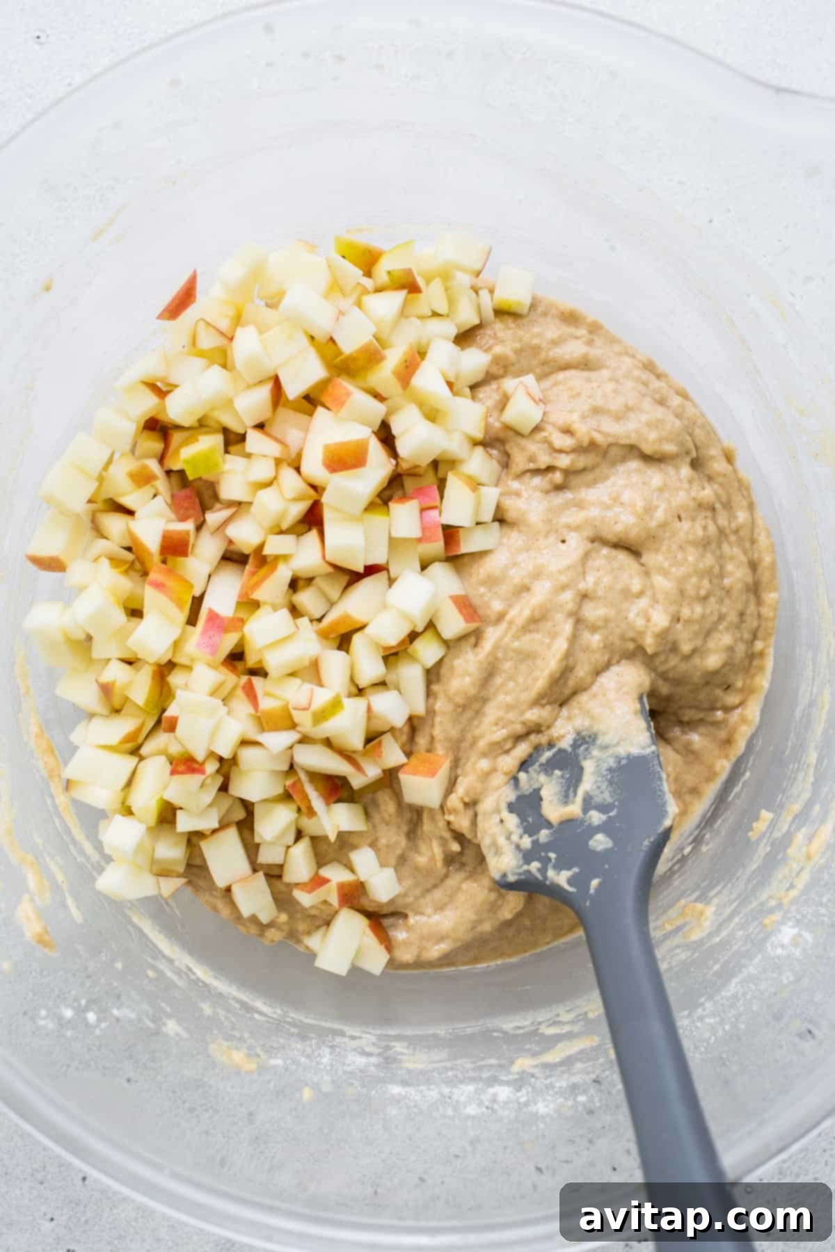 A ceramic bowl filled with freshly diced apples, ready to be added to the muffin batter, with a spatula waiting nearby.