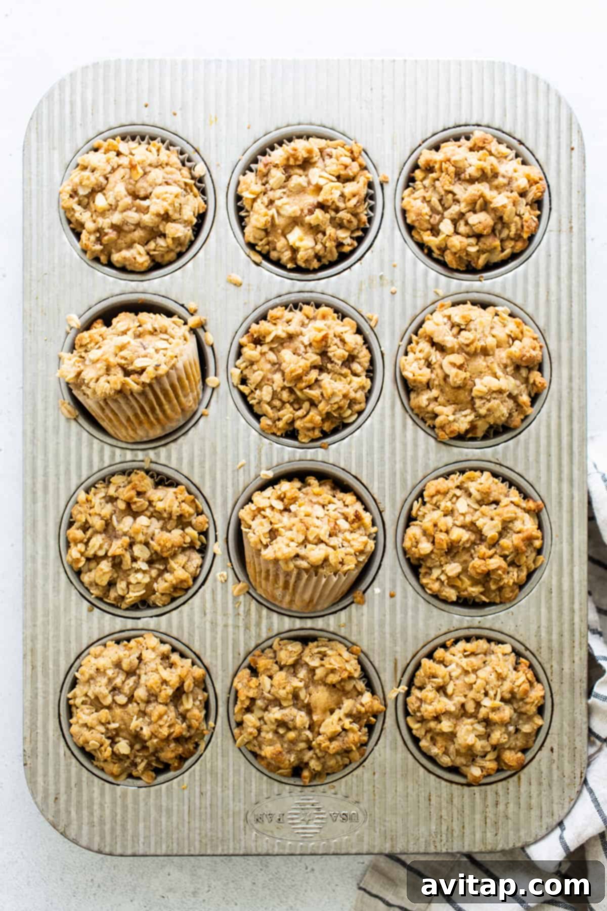A muffin tin filled with freshly baked oatmeal muffins, their delicious streusel tops visible and golden brown.