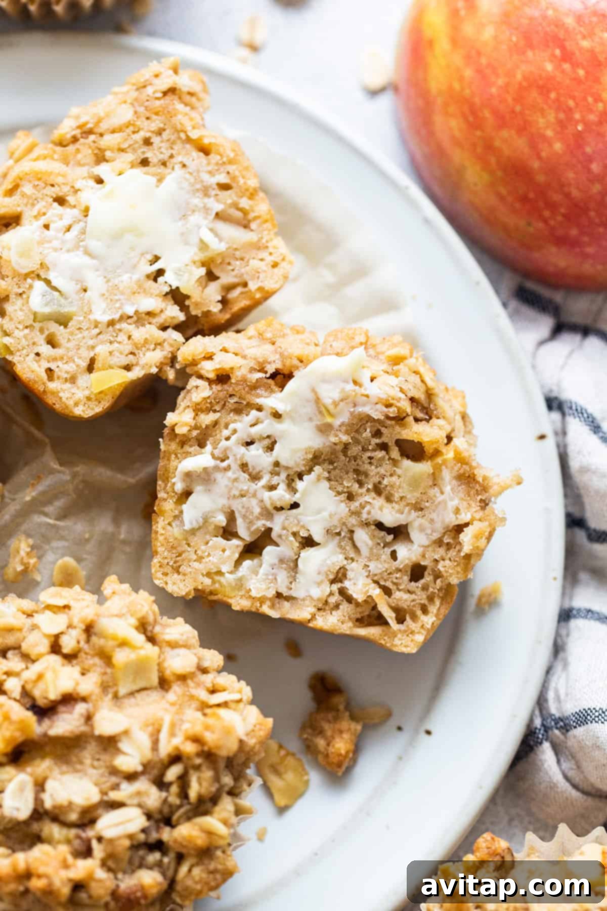 Two warm, inviting oatmeal apple muffins presented beautifully on a white plate, with fresh apples arranged decoratively around them.