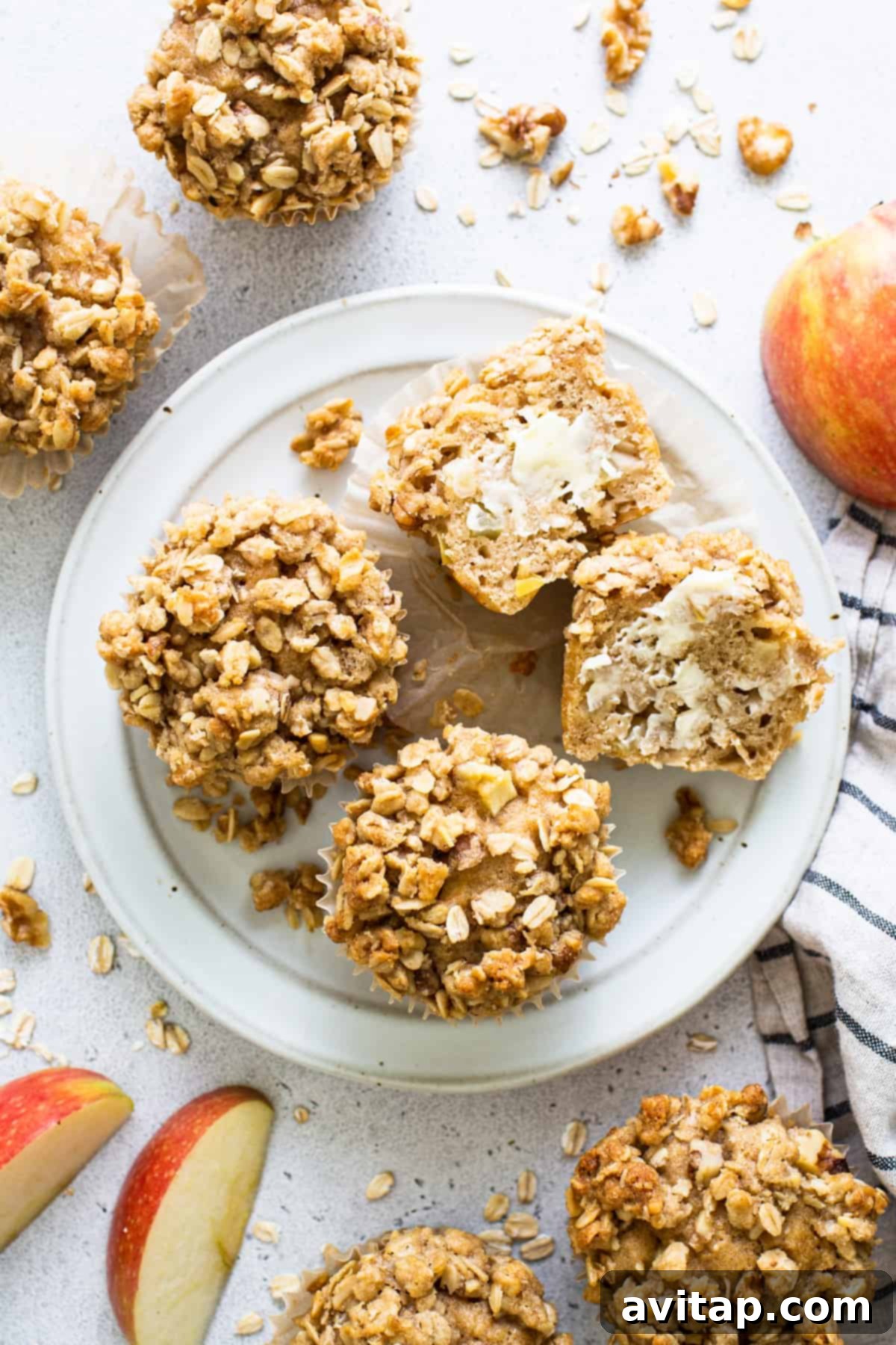 A charming close-up of two oatmeal apple muffins on a rustic plate, with an artful display of fresh apples in the background.