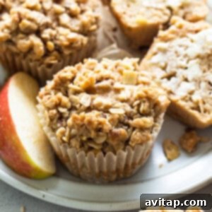 A close-up of a fully baked apple coffee cake muffin with a generous streusel topping, sitting on a white background.