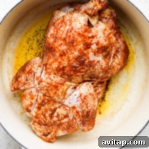 A whole roasted chicken browning in a skillet on a white background.
