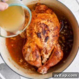 A person pouring liquid over a whole chicken in a pot, preparing for roasting.