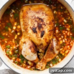 A whole chicken submerged in a pot of Spanish rice and vegetables.