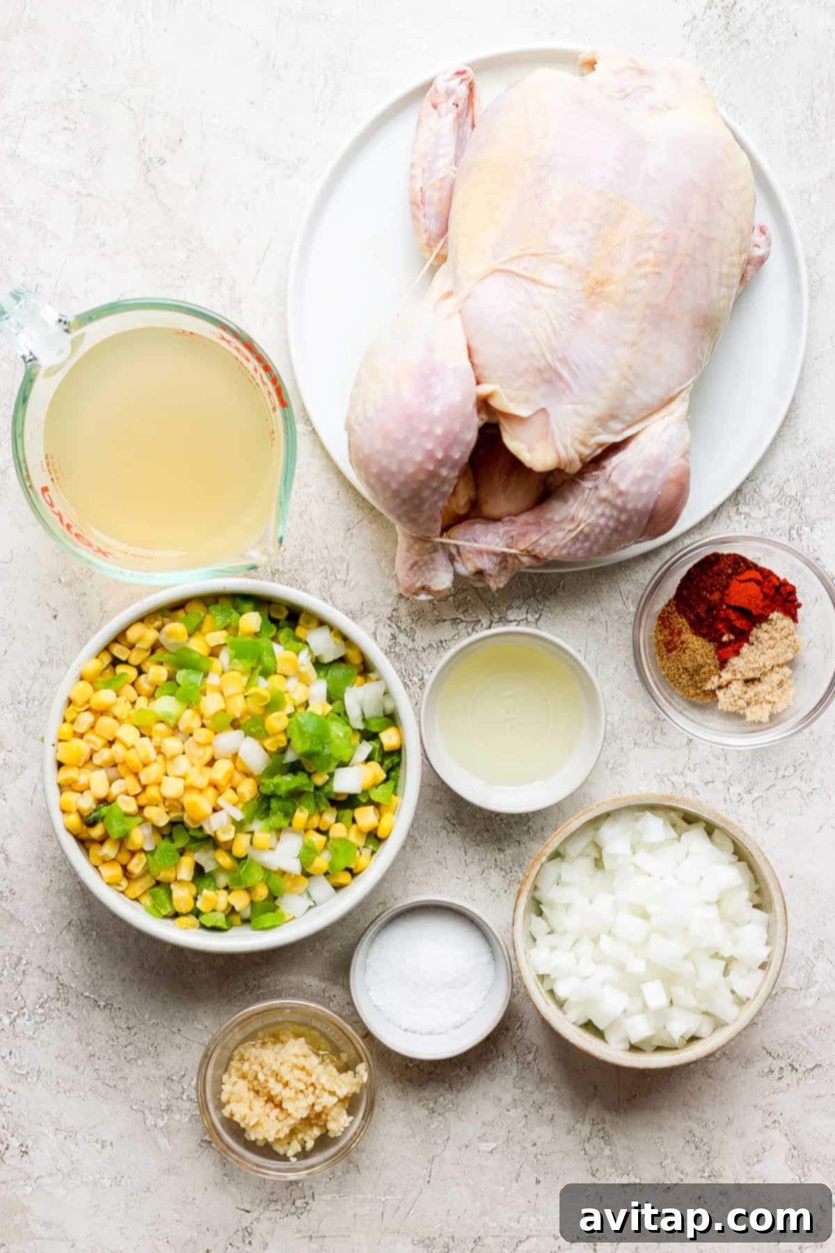 A selection of fresh and pantry ingredients including a whole chicken, corn, onions, and spices, laid out on a table.