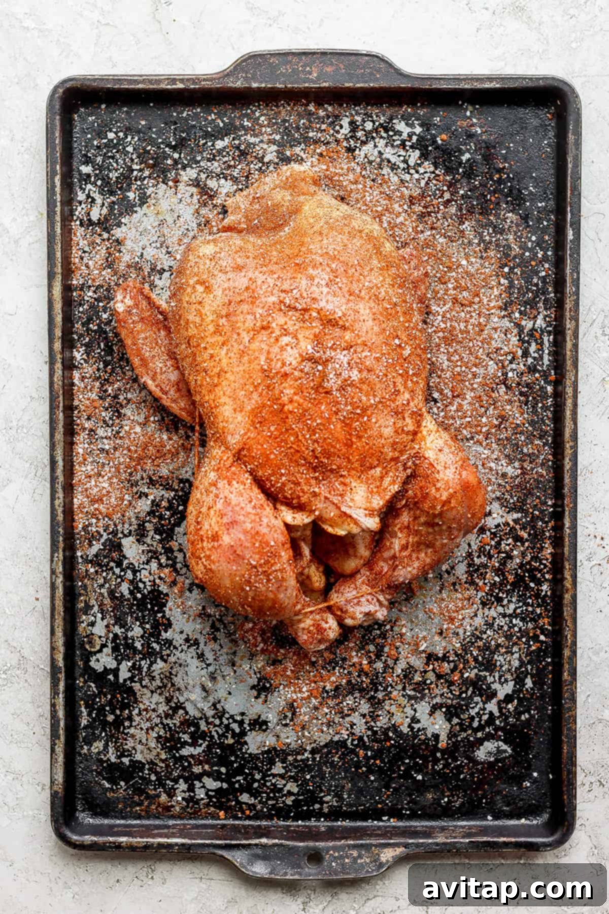 A beautifully roasted whole chicken, golden-brown and crispy, on a baking sheet.