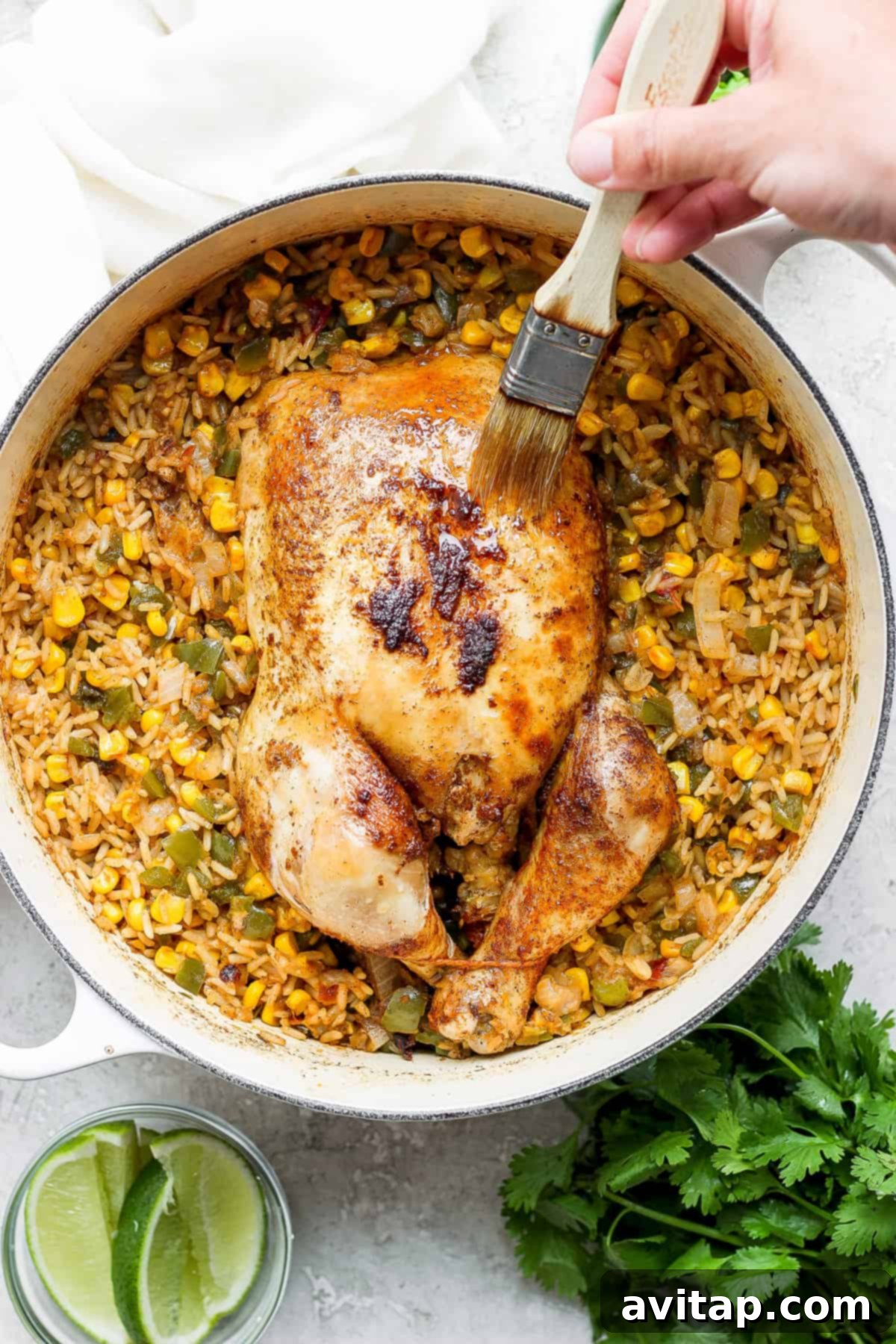 A person is expertly slicing a whole roasted chicken served alongside Spanish rice and corn in a skillet, ready for enjoyment.