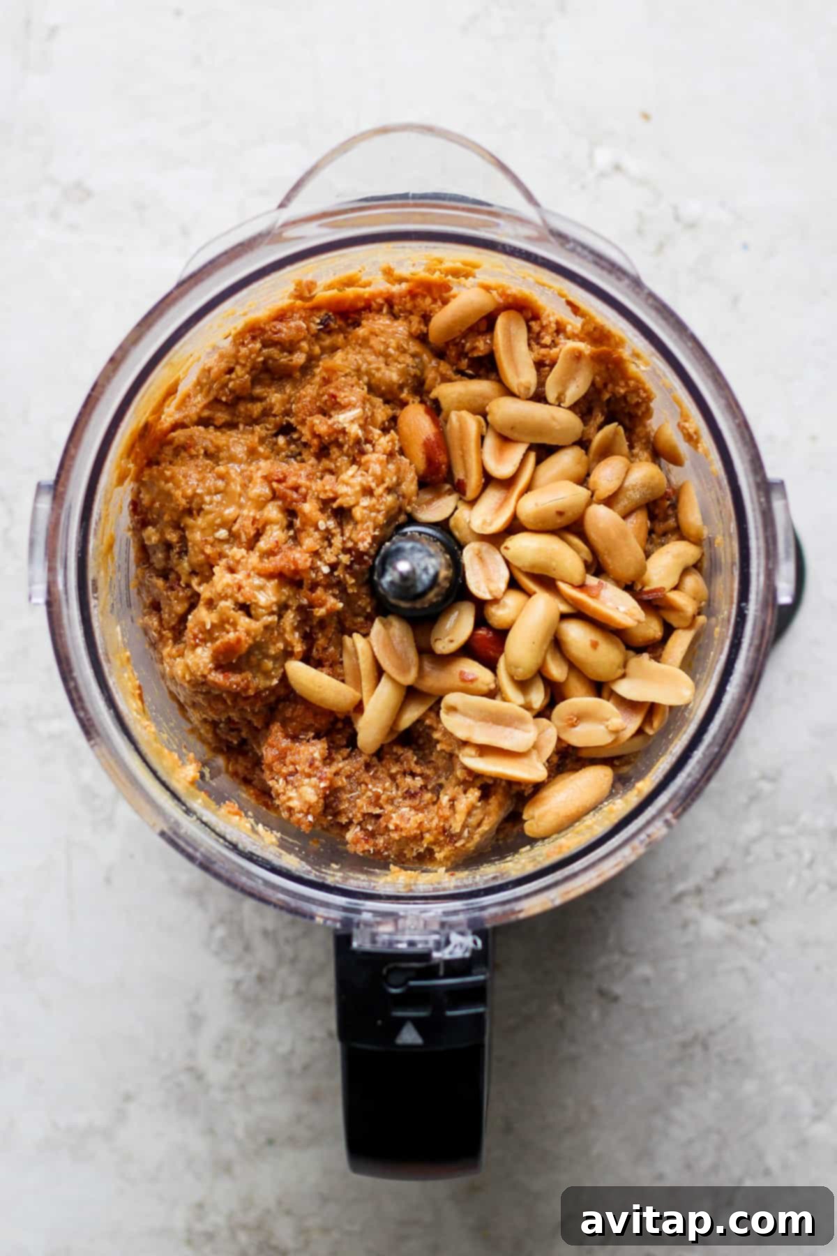 A food processor bowl filled with peanuts and other base ingredients, ready to be blended for Snickers Energy Balls.