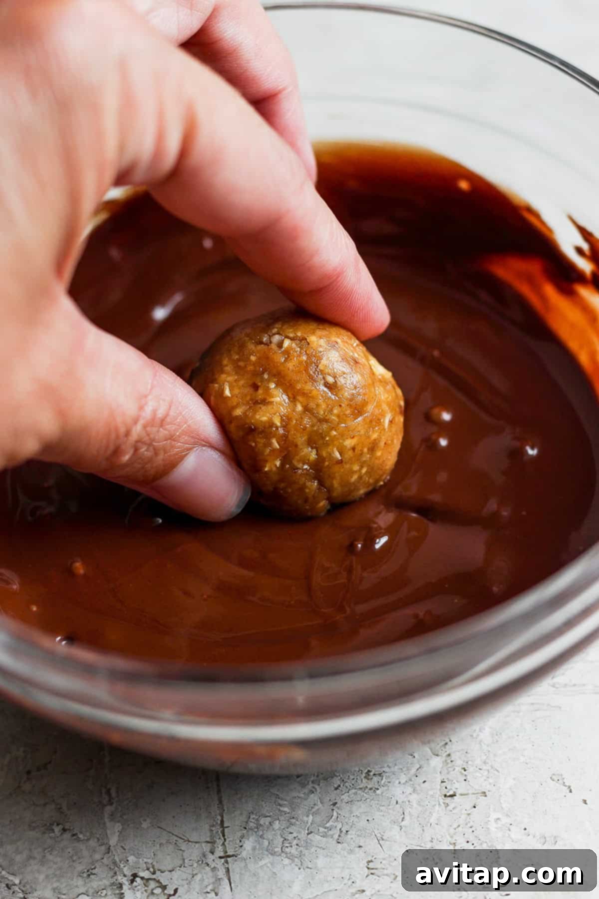 A person dipping a peanut butter and chocolate energy ball into melted chocolate sauce, highlighting the indulgence of the Snickers Energy Balls.