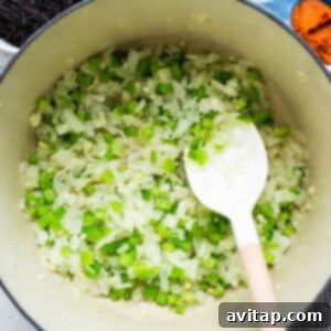 Sautéed onions, garlic, and celery in a pot with a wooden spoon.