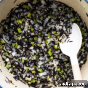 Uncooked wild rice tossed with sautéed vegetables in a pot.