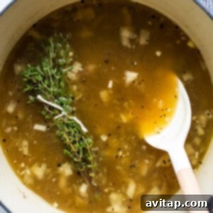 A pot of soup simmering with a wooden spoon and a sprig of fresh thyme.