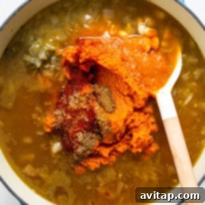 A pot of creamy pumpkin soup simmering, with a wooden spoon.
