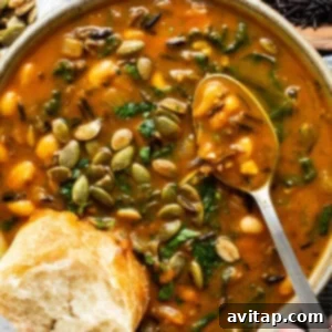 A bowl of creamy pumpkin wild rice soup, garnished with pepitas and served with fresh bread.