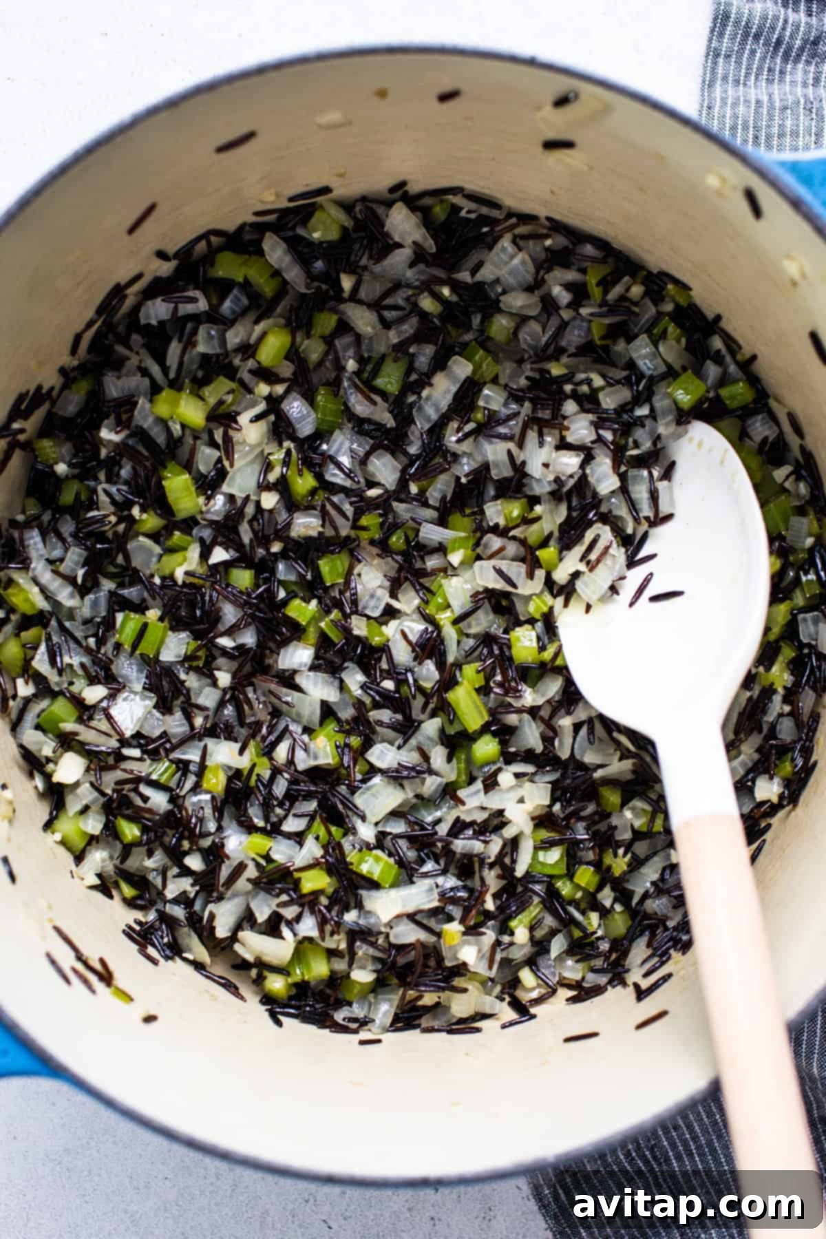 Close-up of uncooked wild rice in a pot with a wooden spoon, ready to be toasted.