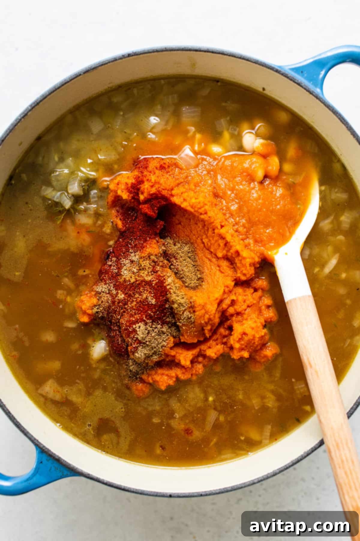 A pot of creamy pumpkin wild rice soup simmering, with a wooden spoon resting inside.