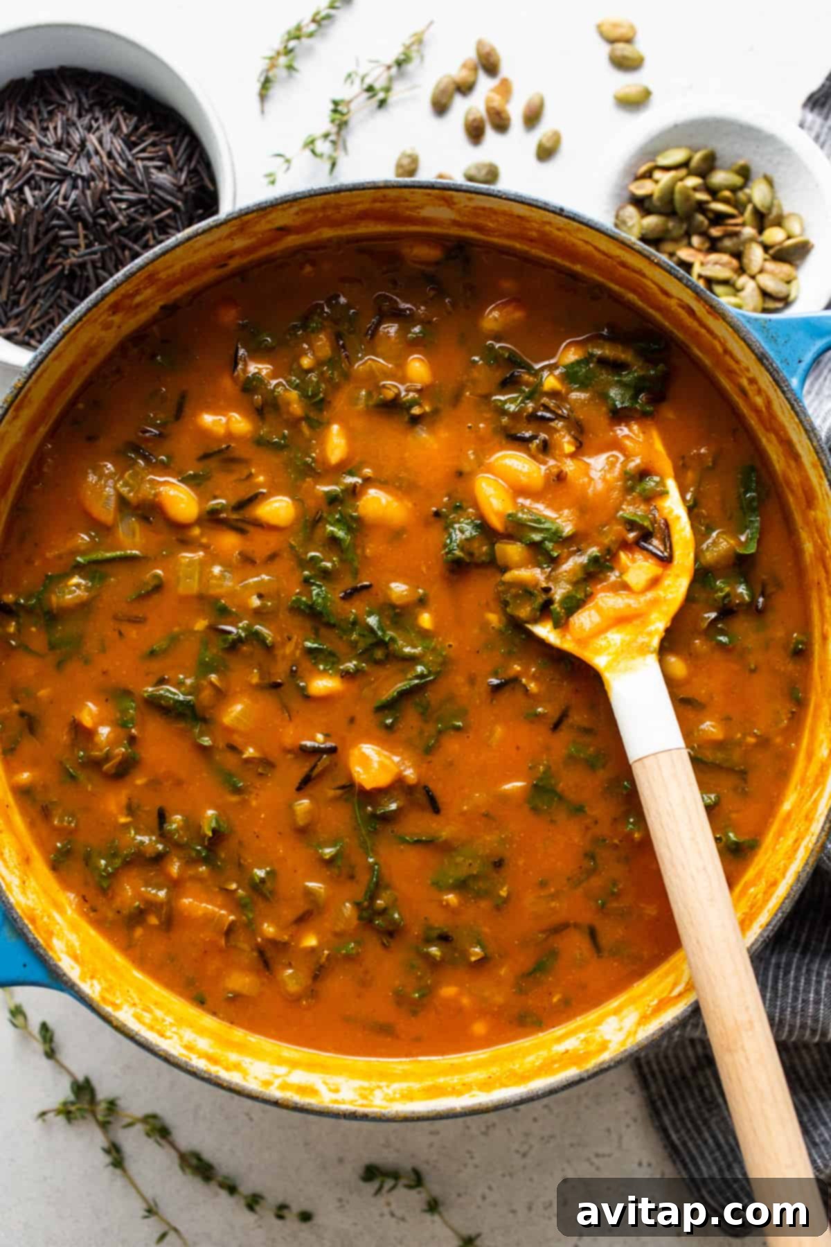 A large pot of rich creamy pumpkin wild rice soup with a wooden spoon, ready to be served.