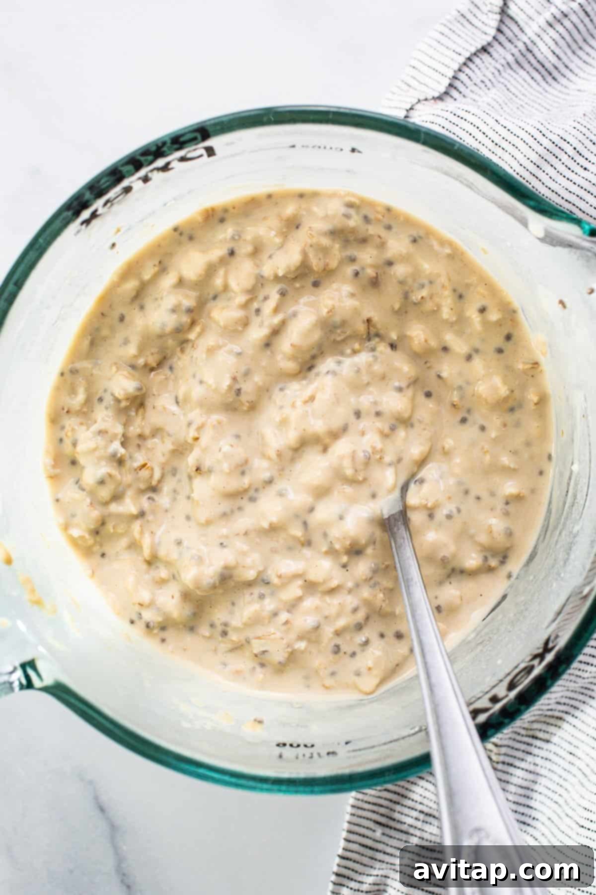 Protein Overnight Oats Three Delicious Varieties 5 A close-up shot of a single bowl of oatmeal, perfectly prepared with a spoon resting inside, showcasing its creamy texture and readiness to be enjoyed.