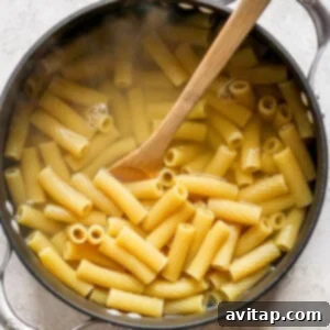 Penne pasta in a pan with a wooden spoon, mid-cooking process.