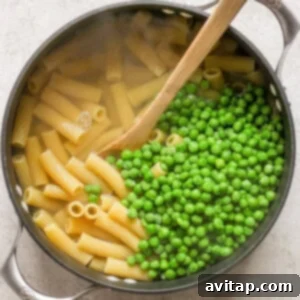 Peas and pasta in a pan with a wooden spoon, cooking together.