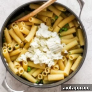 Penne pasta with peas and feta cheese in a skillet, stirring in the cheese.