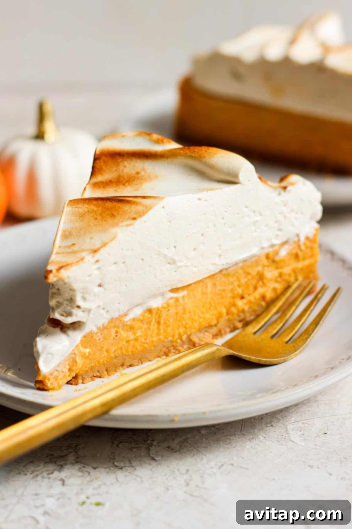 A perfectly sliced piece of high-protein pumpkin cheesecake with a golden fork, showcasing its creamy texture and graham cracker crust.