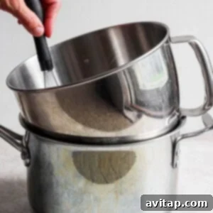 A person using a spatula to stir ingredients in a stainless steel pot.