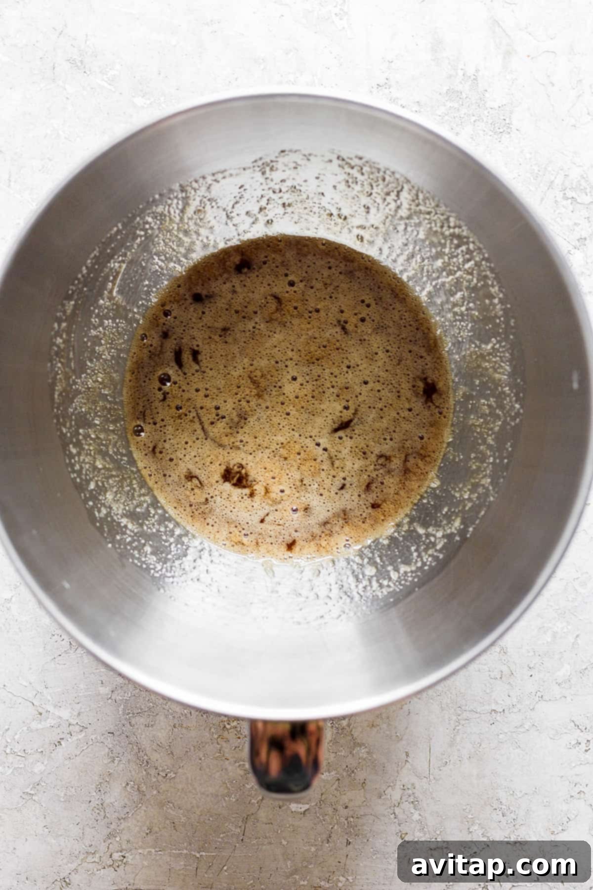 A warm mixture of egg whites and brown sugar in a glass bowl, being gently stirred over a simmering pot of water, part of the double boiler setup.