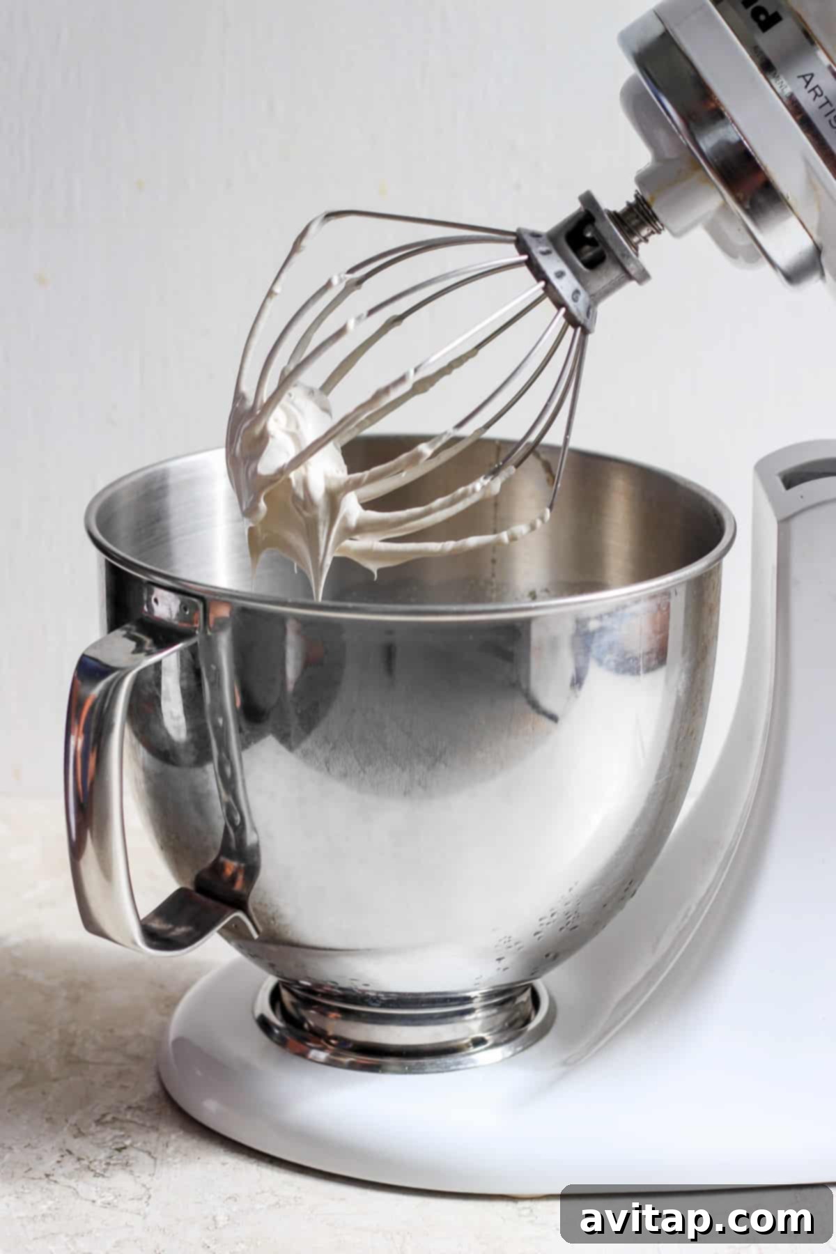 A stand mixer bowl filled with stiff, glossy brown sugar Swiss meringue, with the whisk attachment still in place.