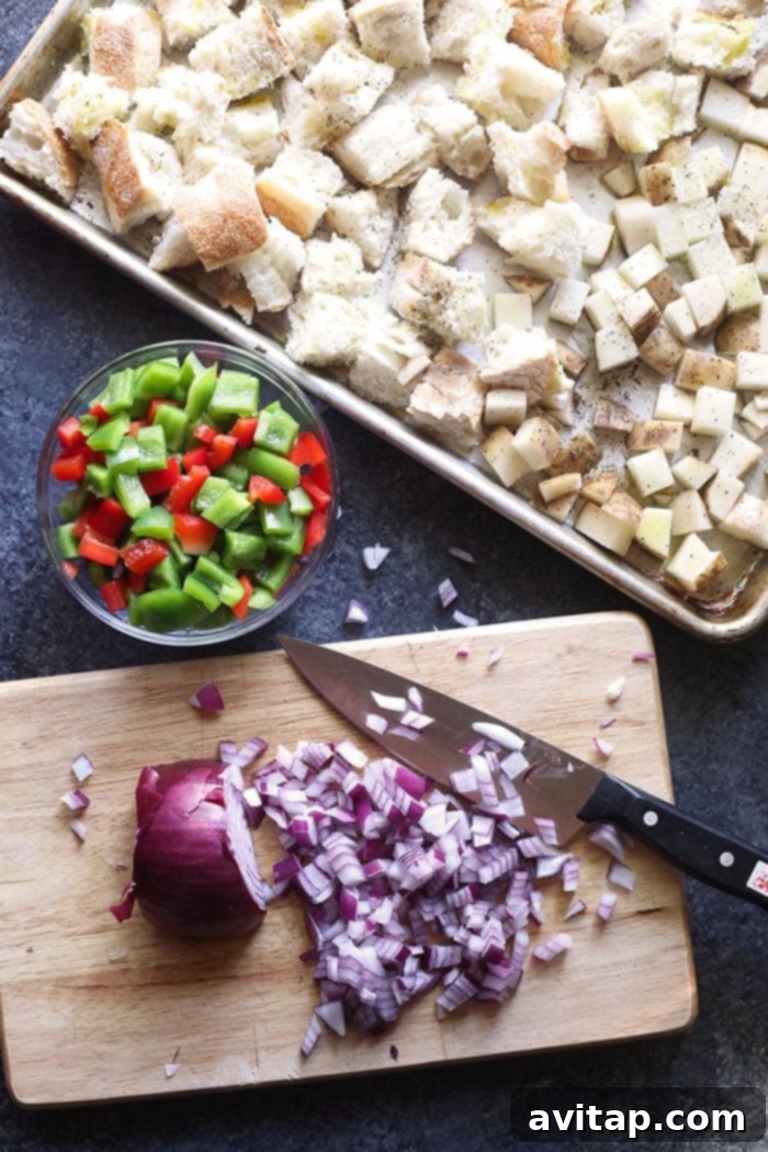 An organized assortment of fresh ingredients laid out for a spicy Italian sausage egg bake, including vibrant bell peppers, purple onions, aromatic garlic cloves, sun-dried tomatoes, creamy goat cheese, farm-fresh eggs, and cubed sourdough bread.